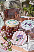 Jug and embroidered drink covers on juice glasses in the garden