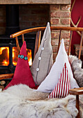 Decorative cushions in the shape of a fir tree on a wooden chair in front of a log fire