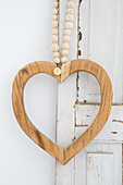 Wooden heart on a string of wooden beads in front of a white door in a shabby chic look