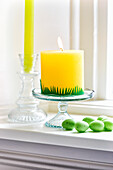 Yellow candle on glass stand with decorative Easter eggs on windowsill