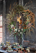 Large autumn wreath of dried flowers, deer head in the centre, stack of books underneath