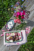 Homemade broken chocolate, bouquet of flowers and rose petals on a wooden bench in the garden