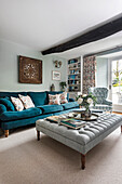 Living room with blue velvet sofa and floral cushions, rustic wooden beams