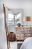 Rustic chest of drawers and bamboo ladder in the bright bedroom with basket