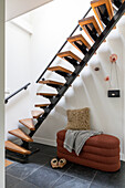 Modern wooden staircase with black metal details, small upholstered bench under the stairs