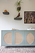 Sideboard with rattan inserts in front of wall with decoration, plant and picture