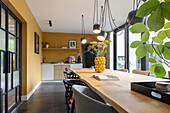 Dining room with long wooden table, yellow walls and modern lighting