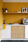Küchenzeile mit Holzpaneel, Kaffeemaschine und gelber Wand mit Regal