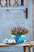 Forget-me-nots in blue Guglhupf mould, tins with lids and meringue on wooden bench in front of door