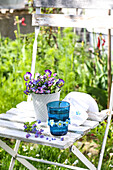Blue glass with DIY decoration, horned violets and forget-me-nots in a flower pot on a wooden chair in the garden