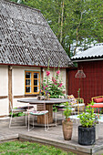 Rural terrace with rustic wooden table and hollyhocks (Alcea) in front of half-timbered house