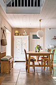 Open-plan cooking and dining area with white vintage cabinetry and light-coloured wooden furniture, kitchen with pastel green cabinets in the background
