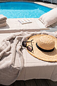 Deckchair with straw hat, towel and sunglasses by the pool