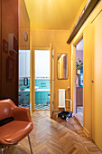 Retro-Flur mit Fischgrätparkett, gelben Wänden und Blick ins türkis gekachelte Bad
