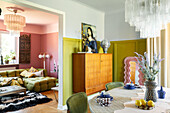 Retro-style dining room adjoining the living room with green sofa and pink-coloured walls