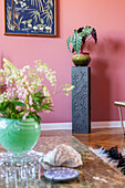 Alocasia in a ceramic pot on a decorative base in front of a pink wall