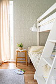 Bright children's room with bunk bed, yellow and white chequered bed linen and stool as bedside table
