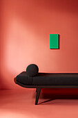 Black daybed in front of coral-coloured wall with green picture