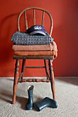 Blankets and cap on wooden chair and rubber boots underneath, red wall