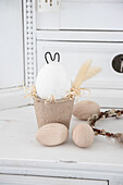 Easter decoration with wooden eggs and bunny figure made of concrete and wire in papier-mâché pot