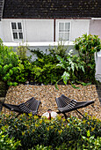 Outdoor area with gravelled area, two black deckchairs and lush planting