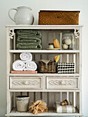 White wooden shelf with towels, baskets and washing utensils