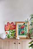 Two flower paintings and vase on wooden chest of drawers