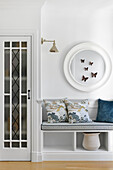 Bench with patterned cushions and round wall mirror with butterfly decoration