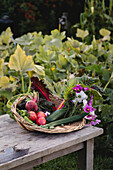 Basket with fresh garden vegetables and flowers on a wooden table in the garden