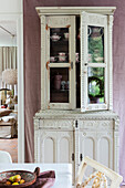 Antique cupboard with crockery against a mauve-coloured wall in the dining room