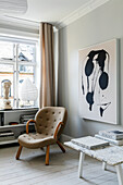 Brown armchair in Scandinavian living room with abstract art and marble table