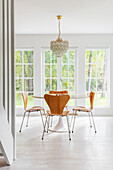 Round dining table with wooden chairs and chandelier in front of large windows