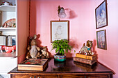 Antique wooden table with bonsai, stuffed animals and books in front of a pink wall