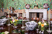 Sumptuously laid dining table with Chinese wallpaper and ceramic decorations on a mantelpiece in the background