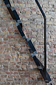 Metal ladder with black railing in front of brick wall