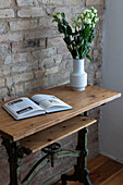 Wooden table with antique base, book and bouquet of flowers, brick wall