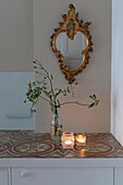 Antique wall mirror with gold frame, flower and candle decoration on a console with patterned tiles