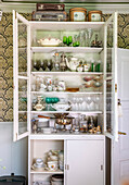 Vintage display cabinet with porcelain and glasses in front of baroque wallpaper