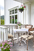 Kleine Landhaus-Veranda mit weißem Holztisch, Metallstühlen und Blumenarrangement