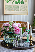 Peonies (Paeonia) and gypsophila in glass vase and candlestick on table