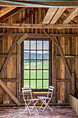 Wooden barn with white metal chairs in front of window with view of landscape