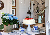 Dining room with blue hydrangea, laid wooden table and cream cake on a cake stand