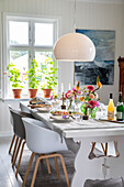 Tastefully laid dining table with bouquets of dahlias and potted plants by the window