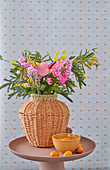 Spring bouquet with flamingo flower (anthurium), hyacinth and mimosa in a woven vase on a round table