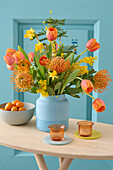 Colourful spring flower bouquet with tulips (Tulipa), pincushions (Leucospermum) and daffodils in a blue vase on a wooden table