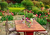 Gartentisch mit Vasen, umgeben von Tulpen auf der Steinterrasse