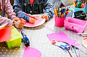 Two children do handicrafts with paper plates and pens on a dotted table