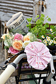 Homemade fabric rosette on bicycle handlebars and bouquet of roses, herbs and newspaper in the bicycle basket