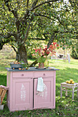 Pink chest of drawers with fern print under an apple tree in an autumn garden