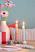 Two marbled stick candles and pink gerbera in vase on wooden table in front of blue diamond wallpaper